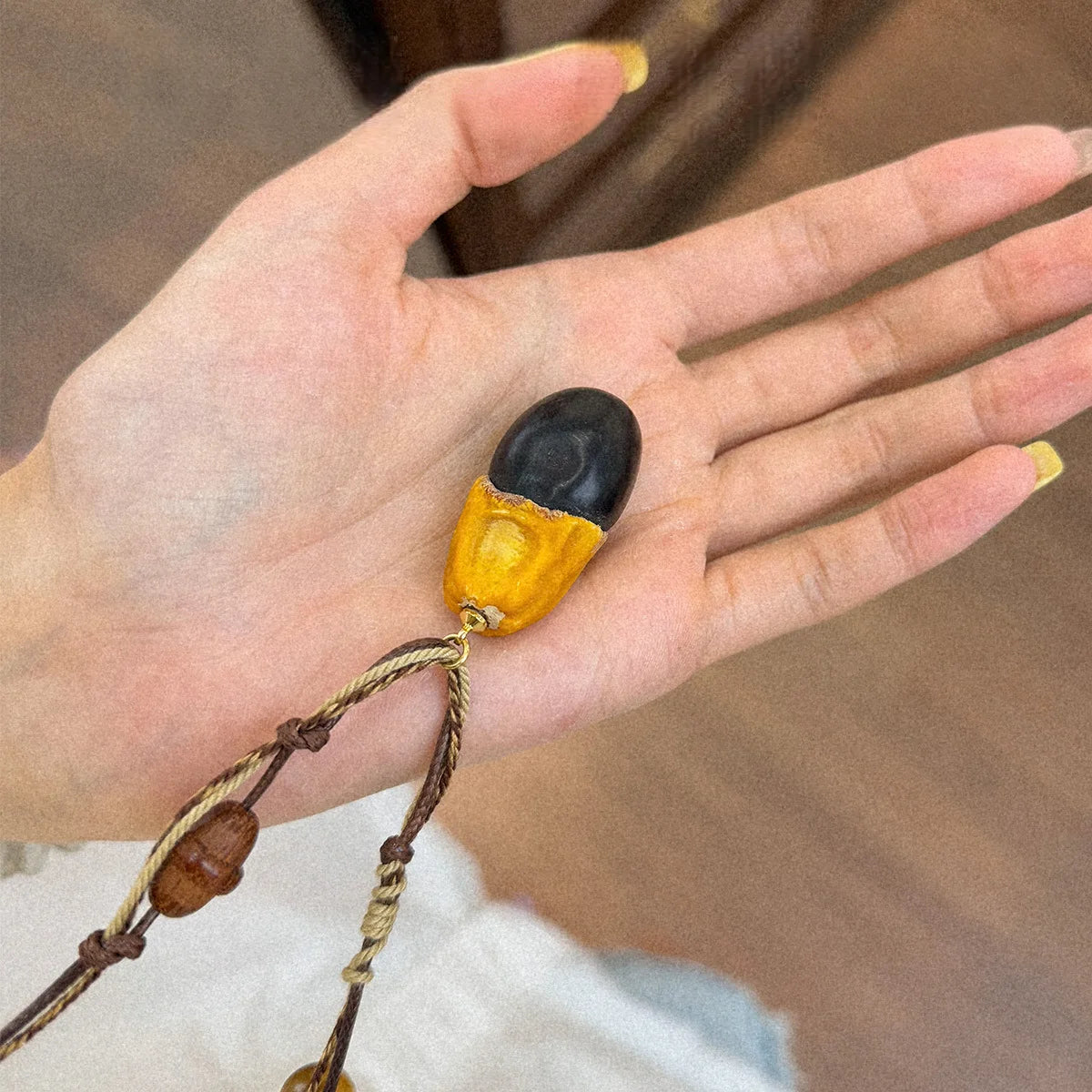 Hand holding boho tiger eye wood pendant necklace with rustic rope cord and natural bead details