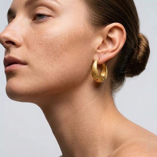 Model wearing gold brushed chunky hoop earrings with a sleek low bun.