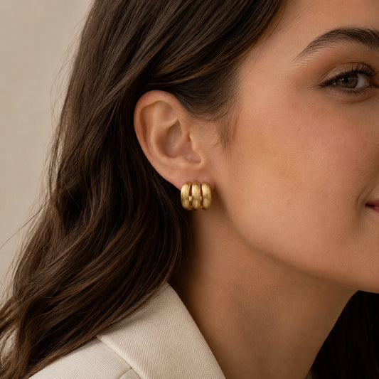 Model wearing gold brushed triple hoop earrings with a neutral tailored outfit.