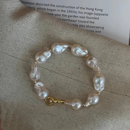Large irregular baroque pearl bracelet with gold accents displayed on natural linen fabric
