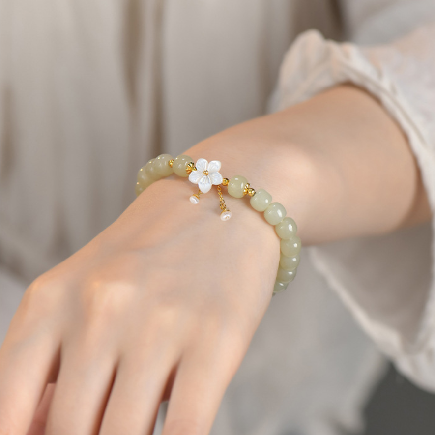 Vintage jade beaded bracelet with mother of pearl sakura charm worn on hand.
