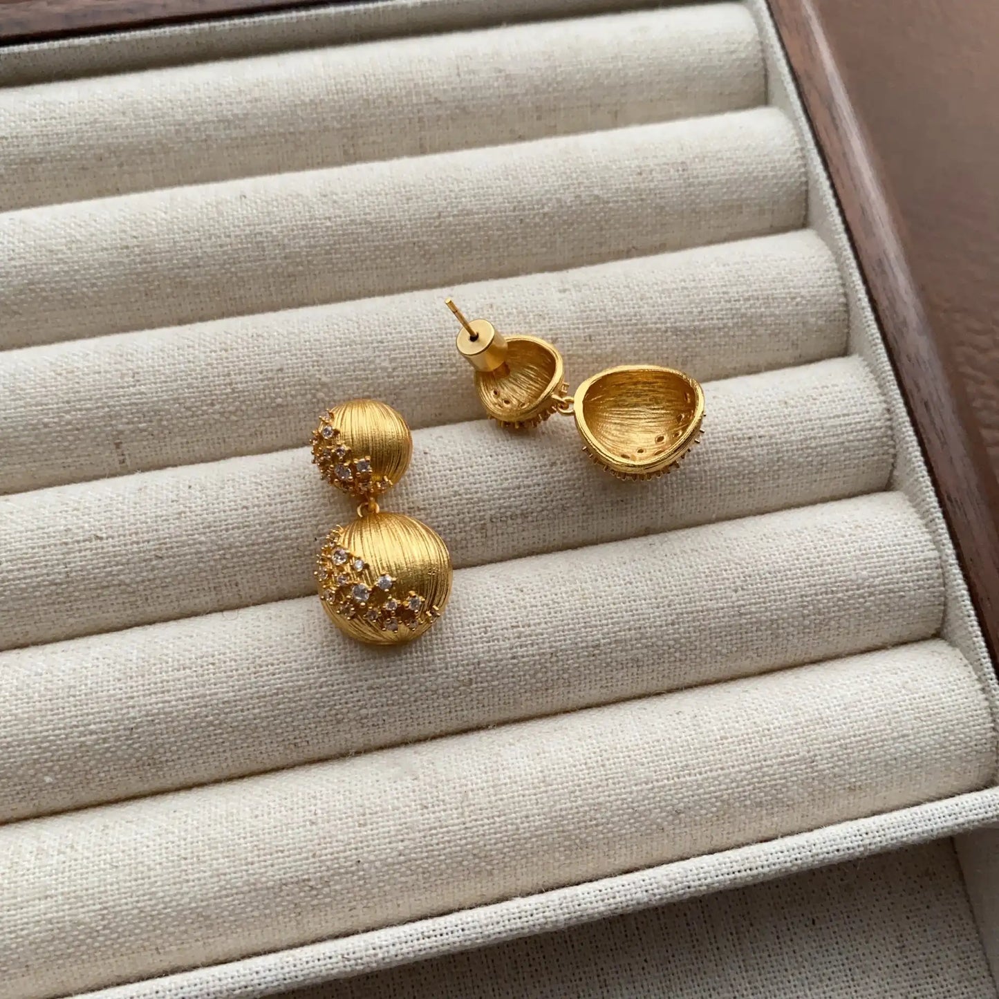 Back and front view of gold textured double ball earrings on a velvet tray