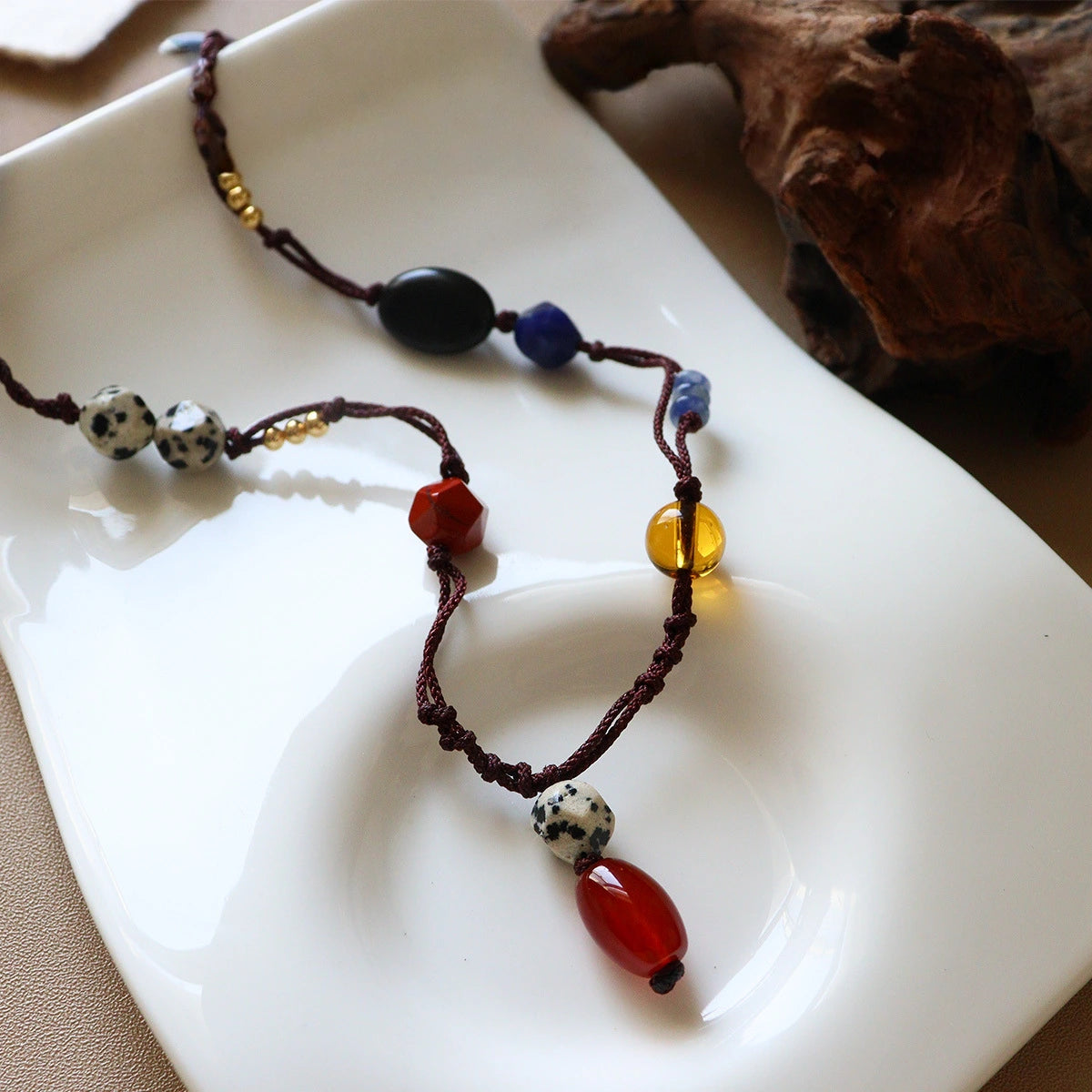 Vintage gemstone rope necklace displayed on white ceramic plate with colorful natural stone beads and brass details