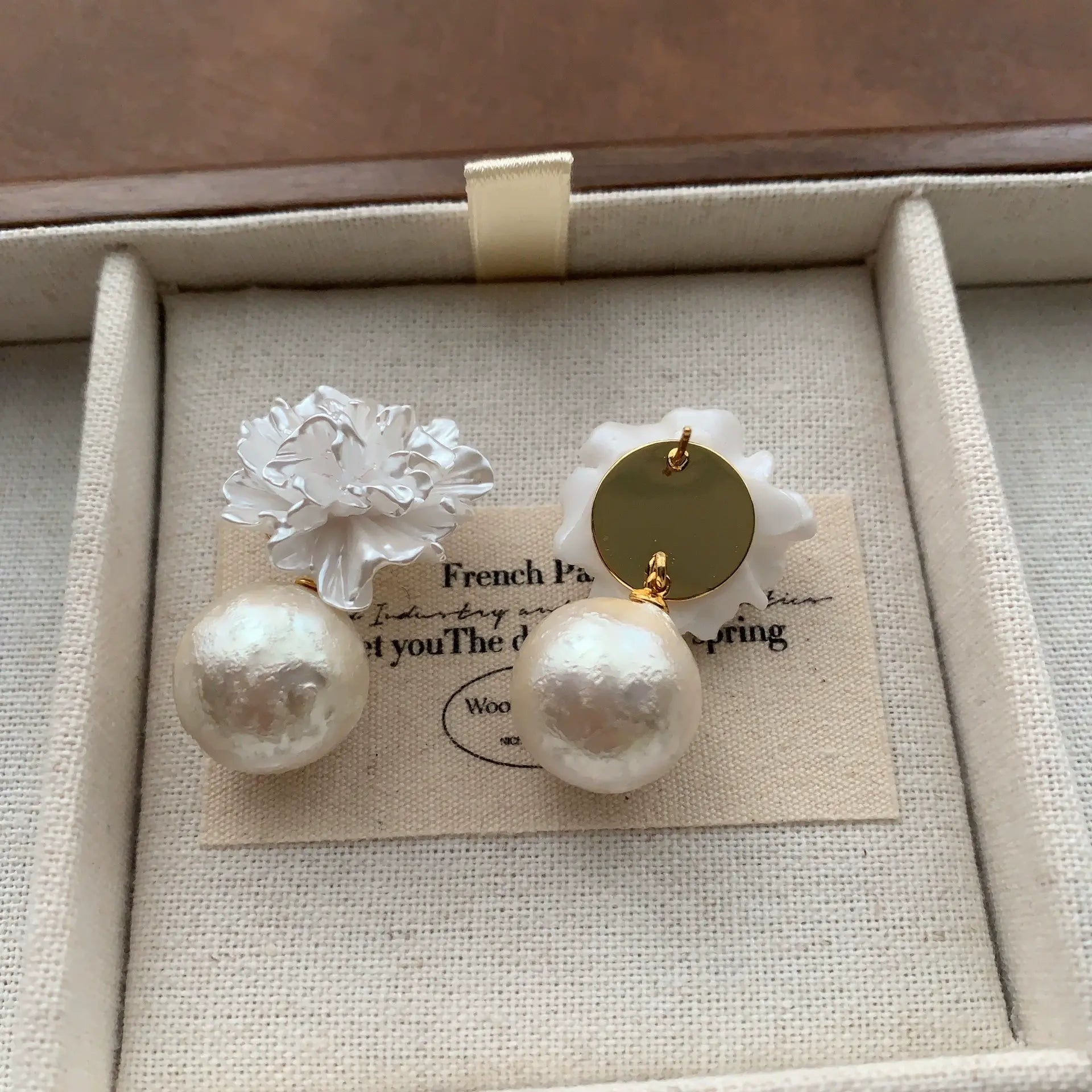 3D white flower pearl earrings displayed on a cream linen jewelry tray.