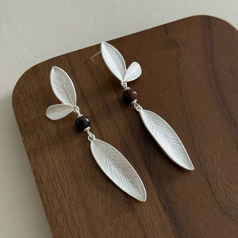 925 sterling silver leaf dangle earrings with dark bead accents displayed on a wooden surface