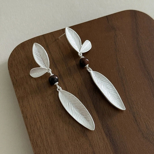 925 sterling silver leaf dangle earrings with dark bead accents displayed on a wooden surface