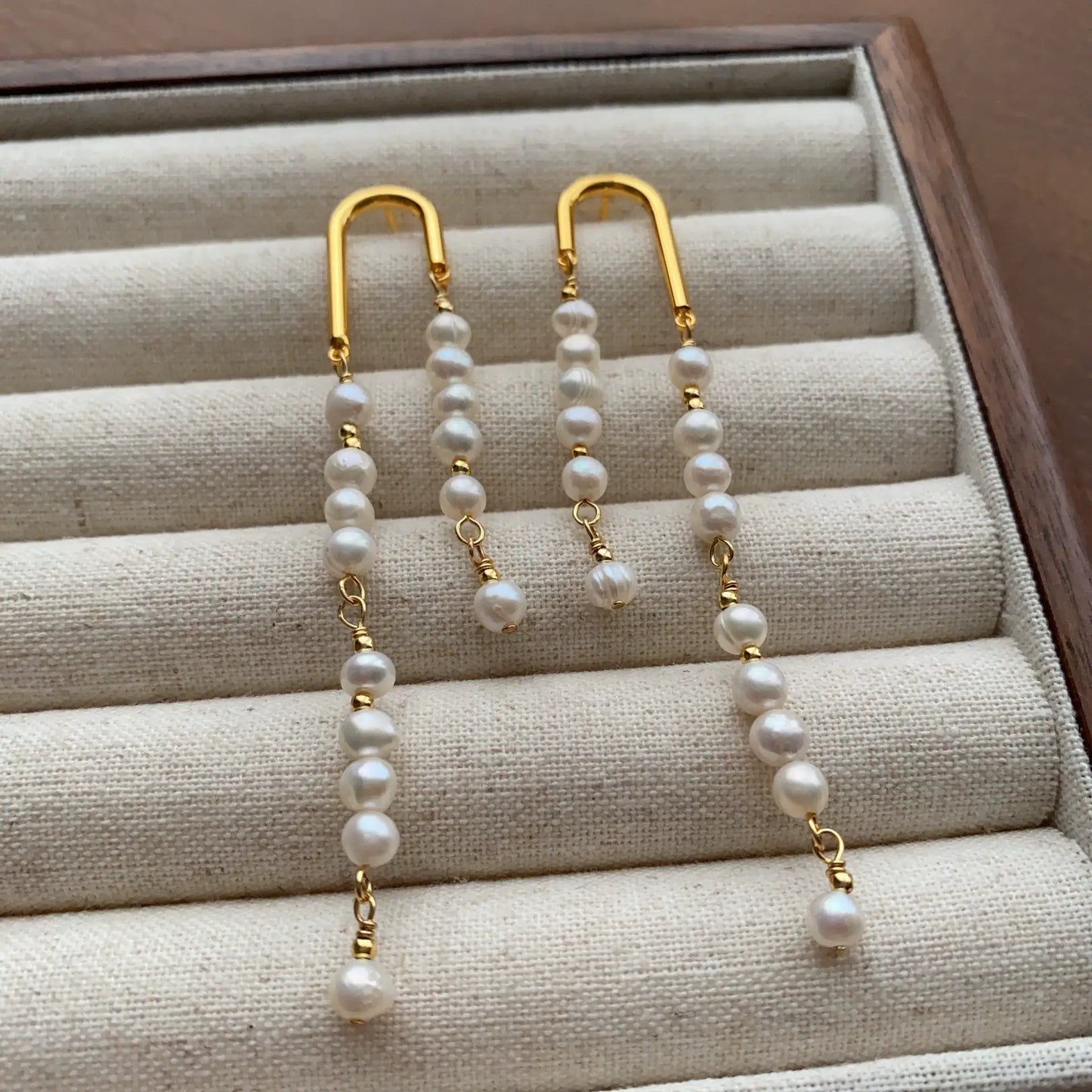 Long mismatched pearl drop earrings with delicate gold-tone arch hooks and cascading pearl strands.