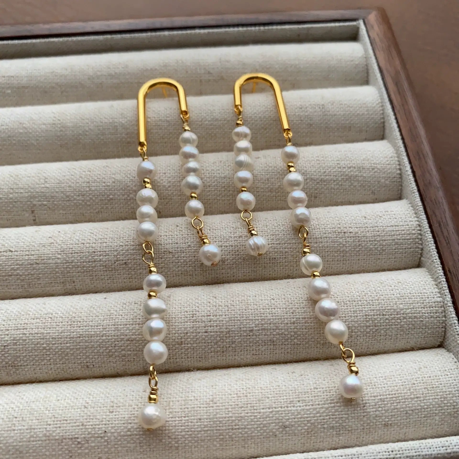 Long mismatched pearl drop earrings with delicate gold-tone arch hooks and cascading pearl strands.