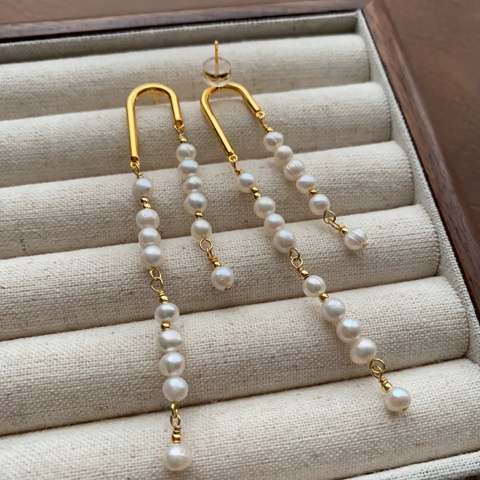 Asymmetric pearl earrings featuring uneven tassel lengths and sculptural gold-tone arches.