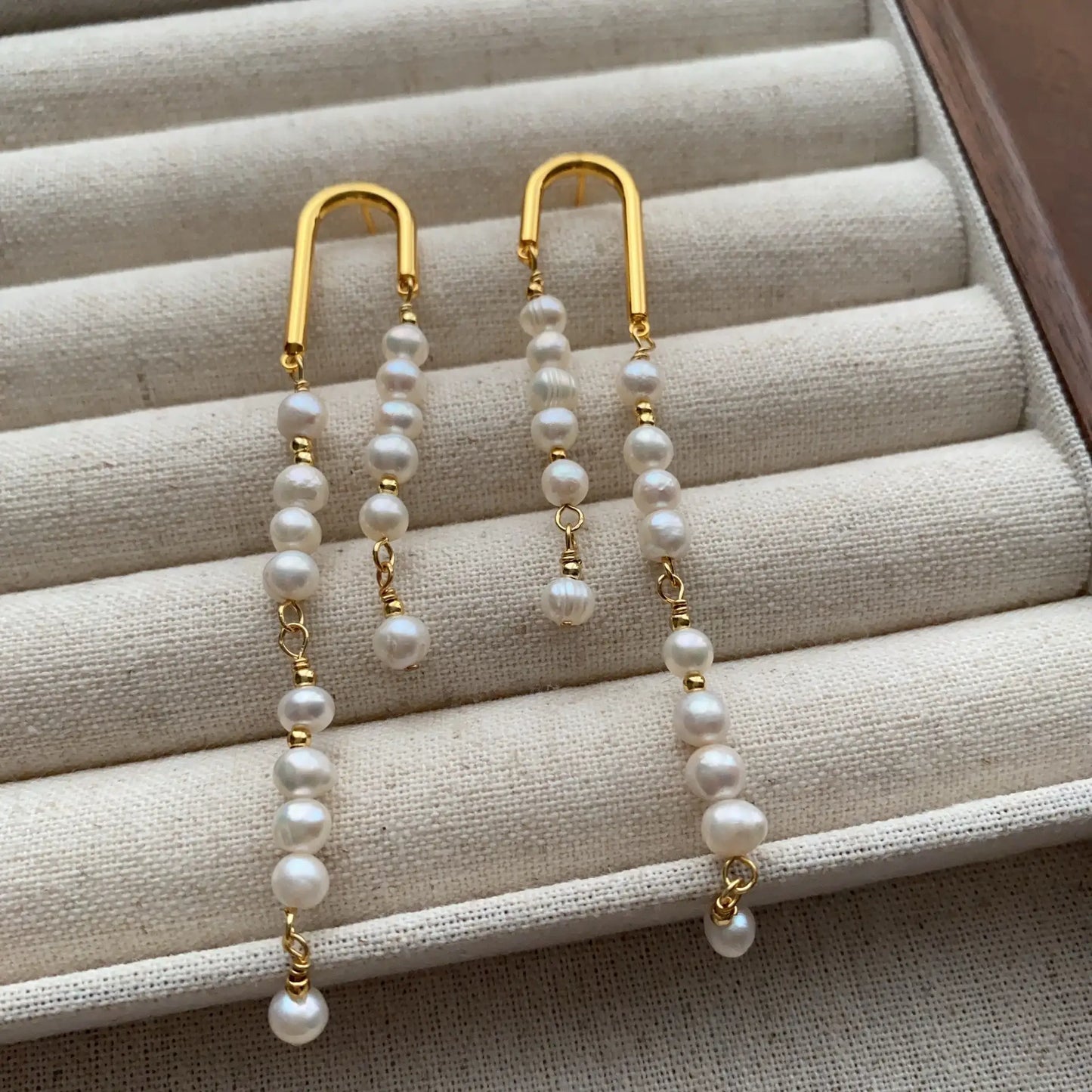 Gold-tone arch pearl tassel earrings arranged in a jewelry box with fluid dangling strands.