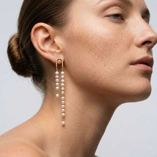 Model wearing long asymmetric pearl tassel earrings with gold-tone arches and a sleek low bun.