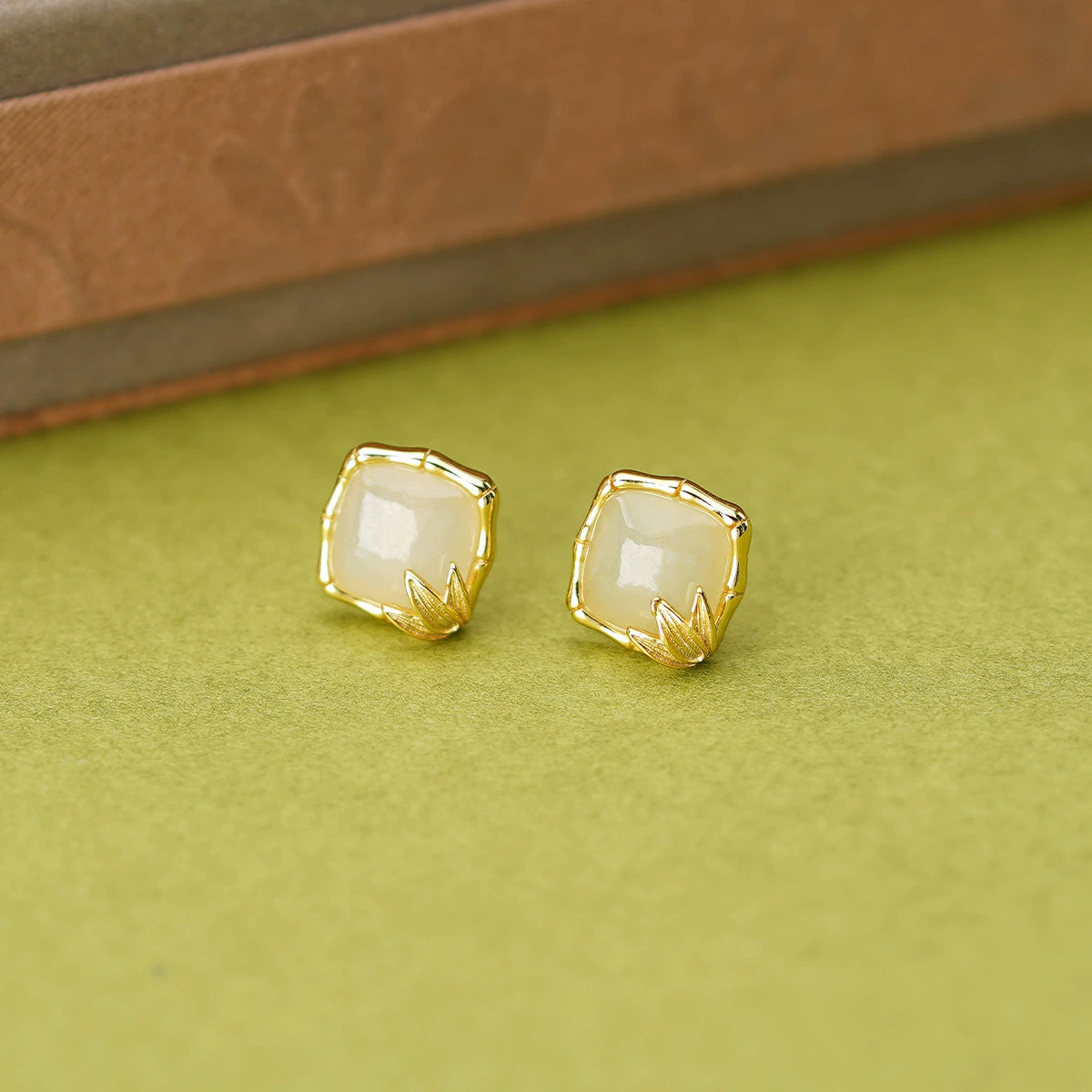 Bamboo frame white Hetian jade stud earrings in S925 silver on a green display