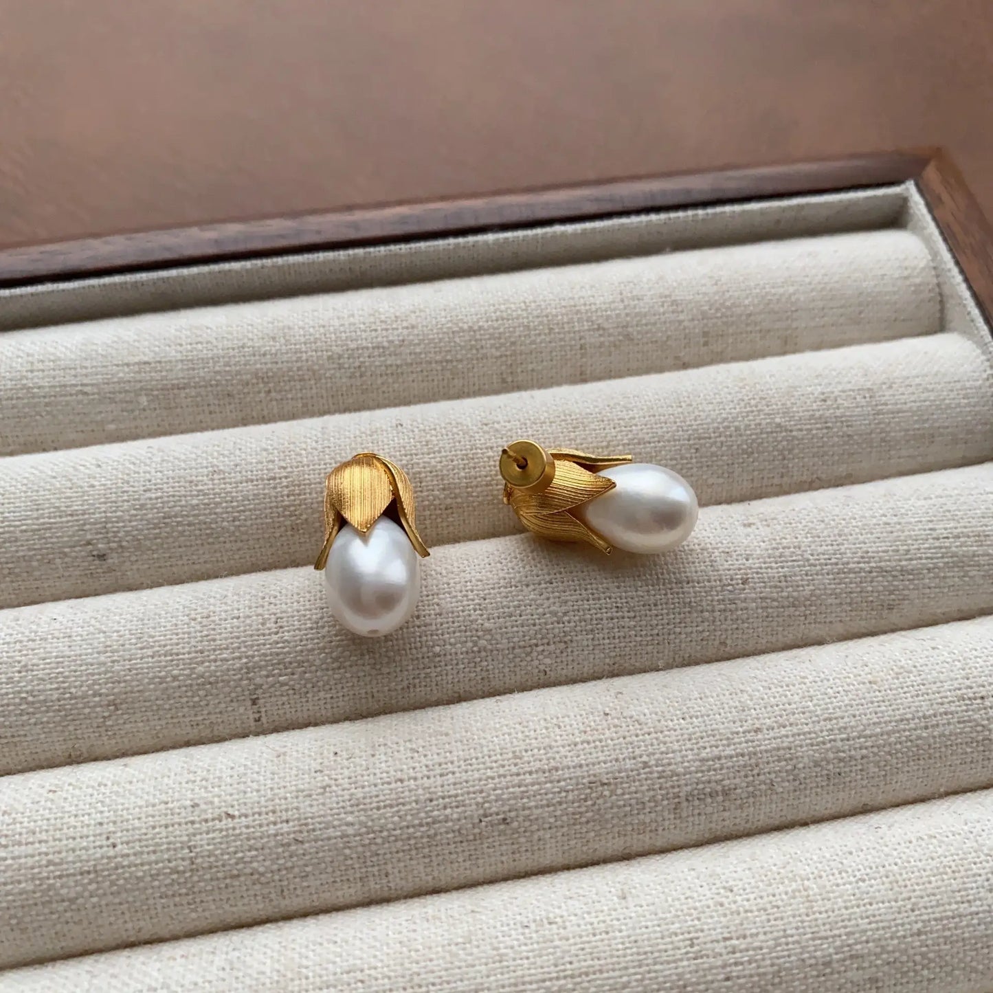 Angled view of gold baroque pearl bud stud earrings on a cream velvet display
