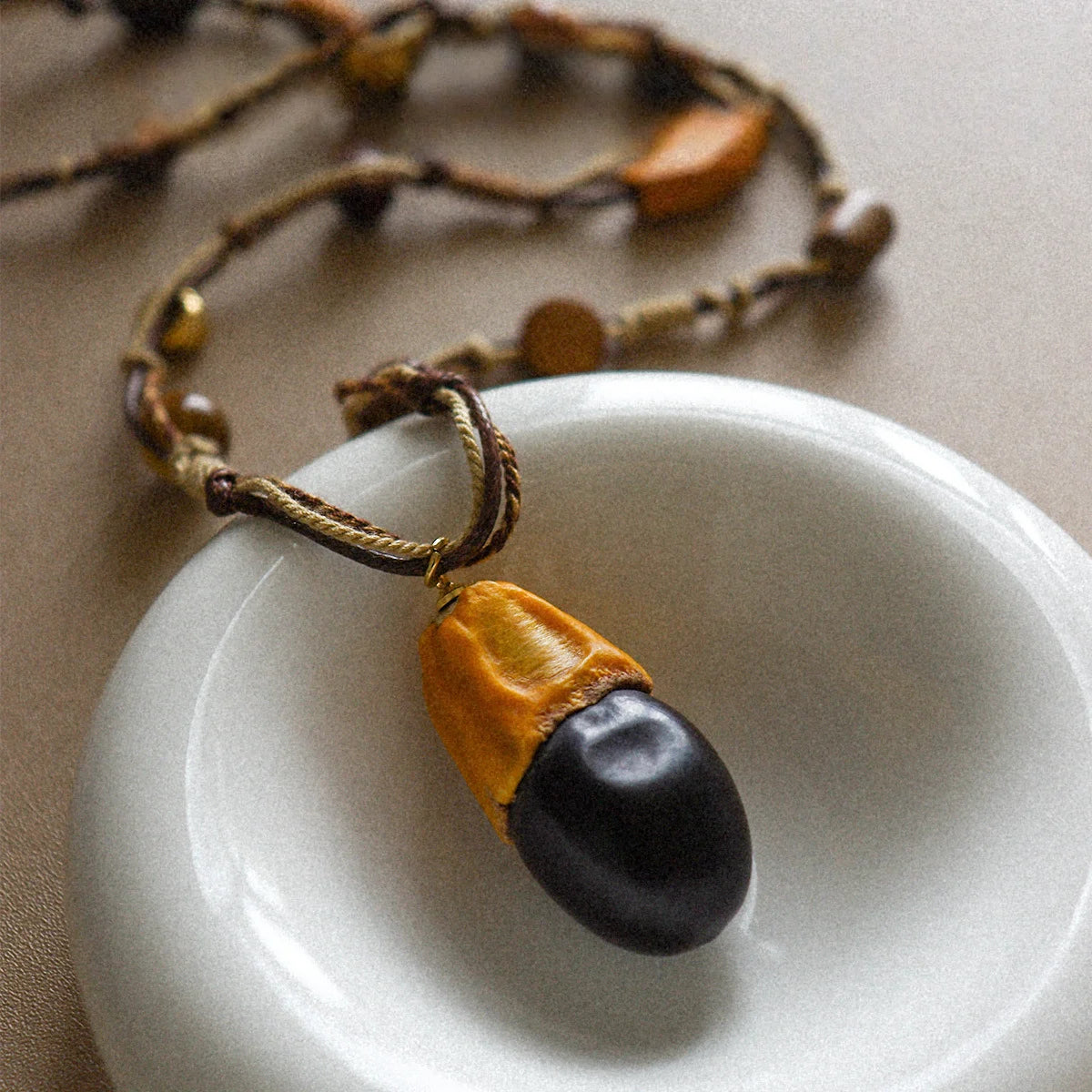 Close-up of tiger eye and wood pendant necklace with bohemian rope cord on a white ceramic dish