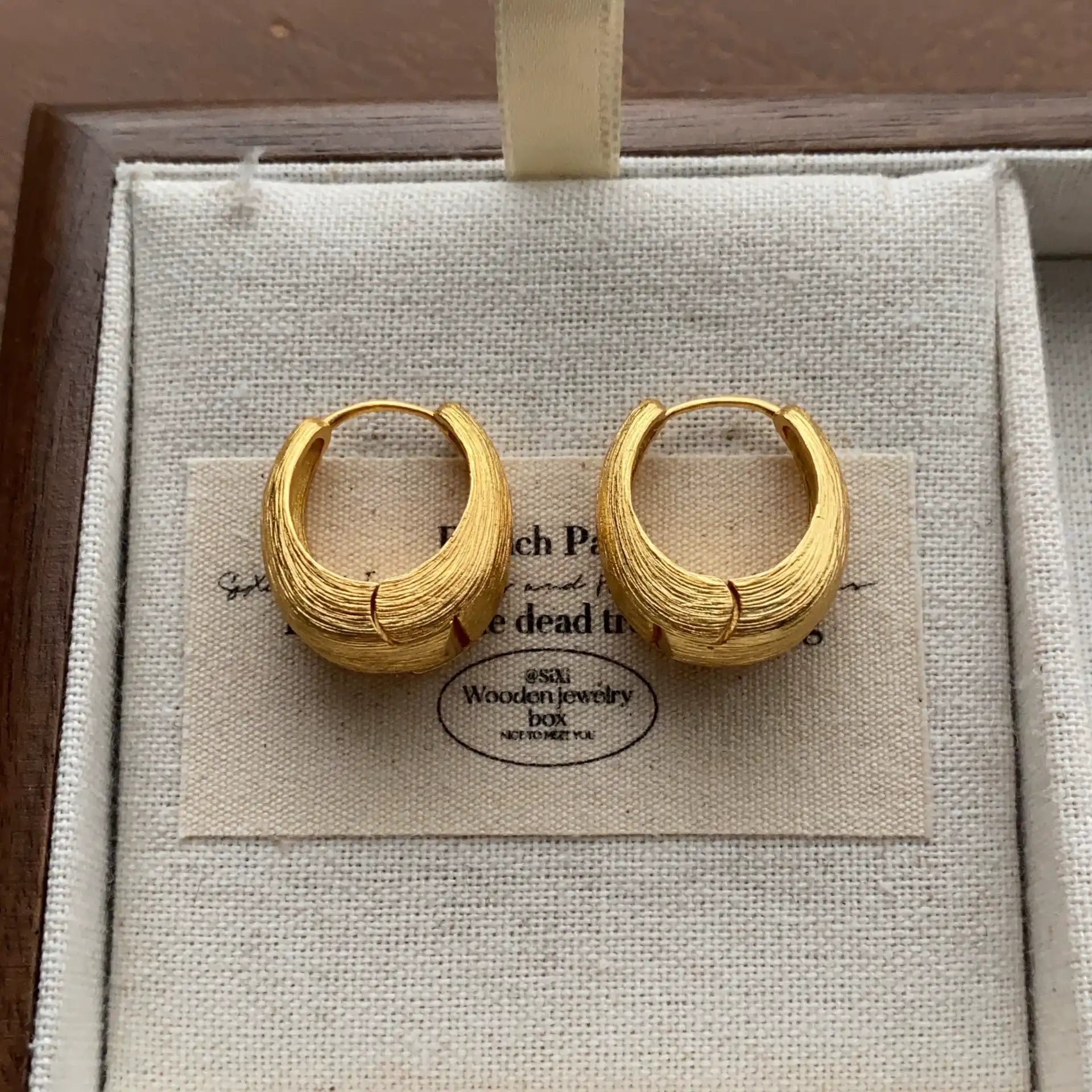 Gold-tone brushed chunky hoop earrings displayed on a cream linen jewelry tray.