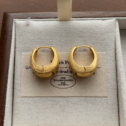 Gold-tone brushed chunky hoop earrings displayed on a cream linen jewelry tray.