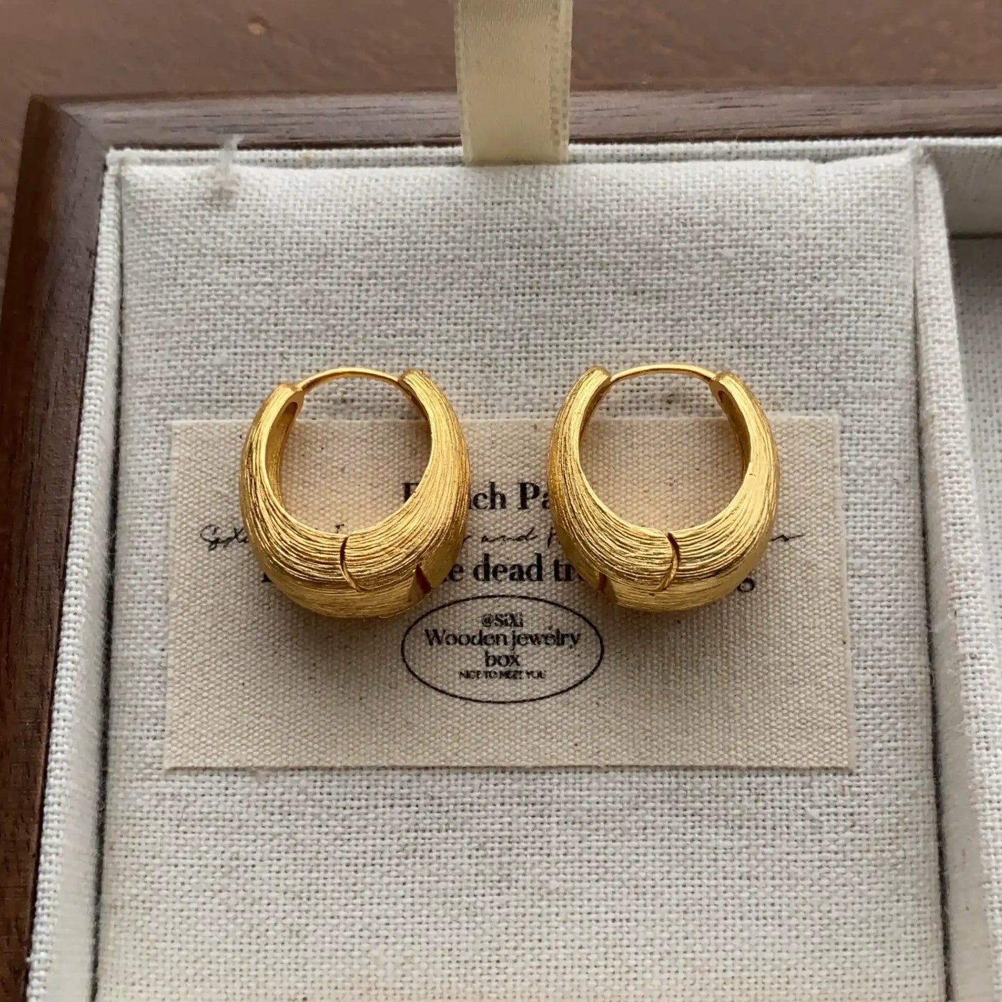 Close-up of gold-tone chunky hoop earrings with a brushed metal texture.