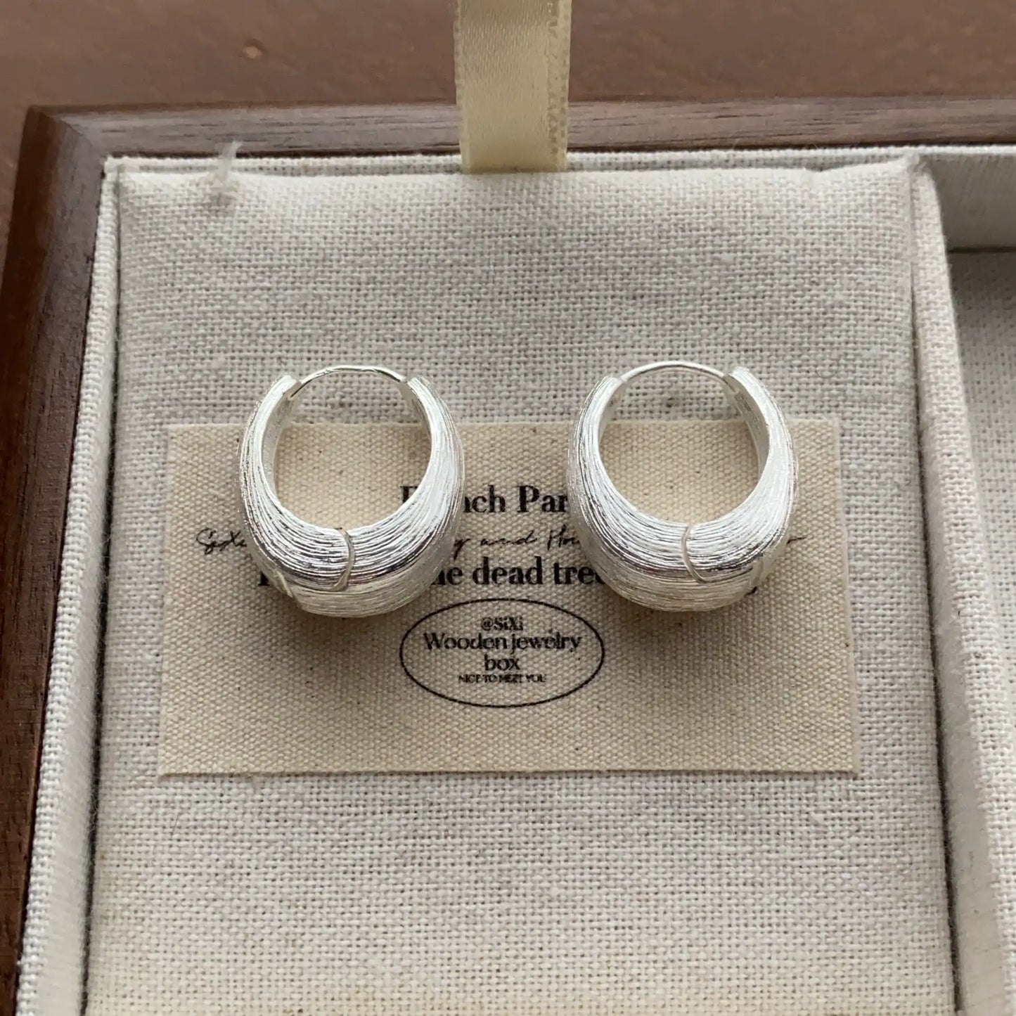 Close-up of silver-tone chunky hoop earrings with a sculptural rounded profile.