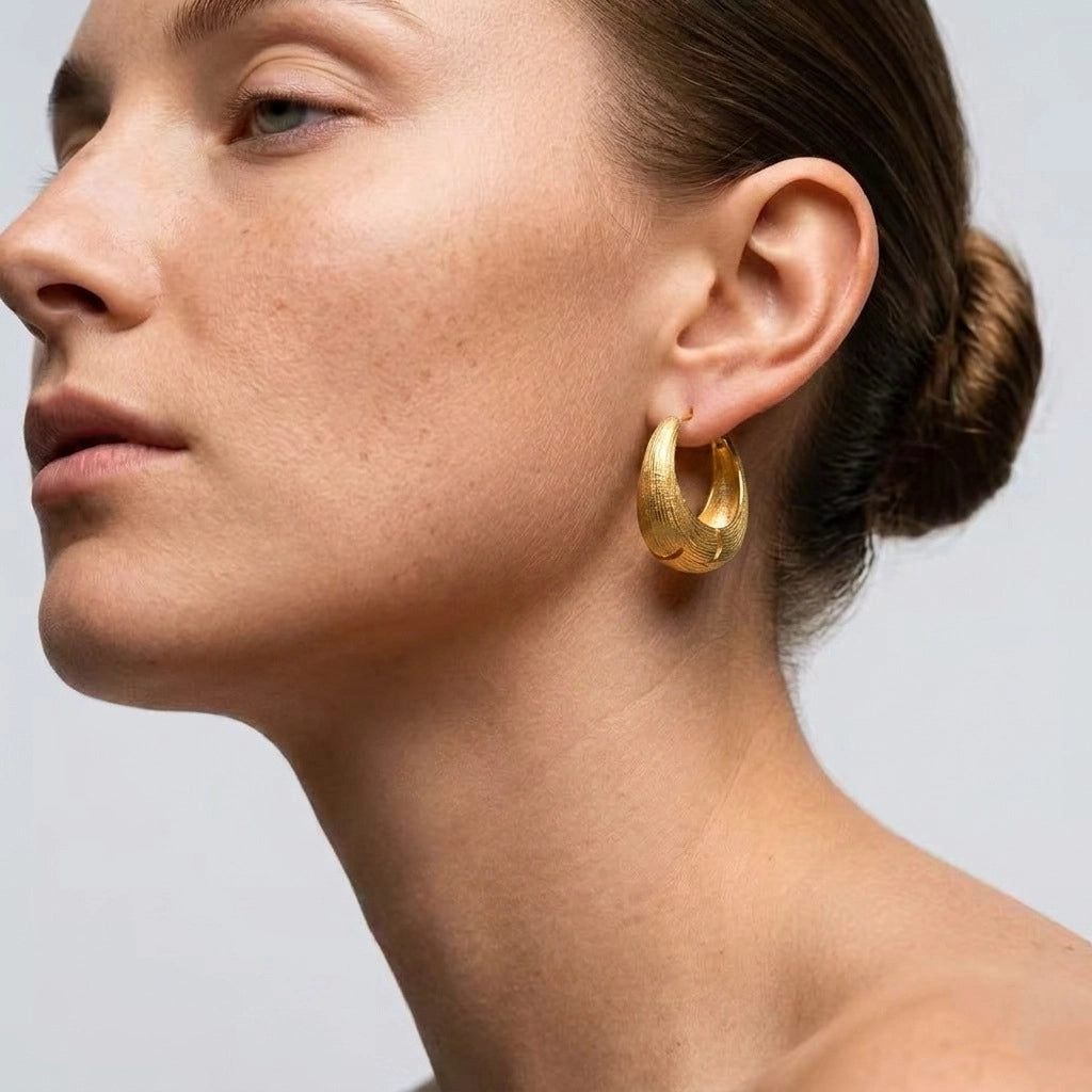 Model wearing gold brushed chunky hoop earrings with a sleek low bun.