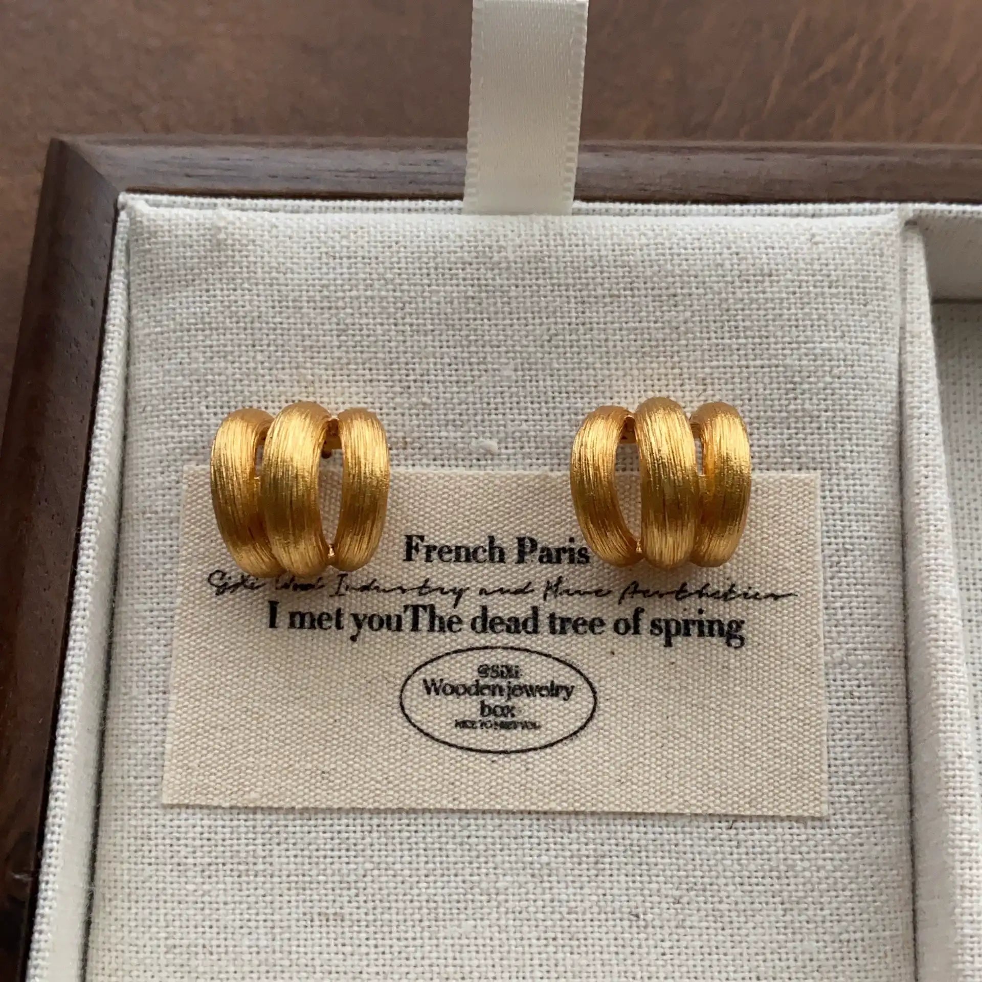 Gold-tone brushed triple band hoop earrings displayed on a cream linen jewelry tray.