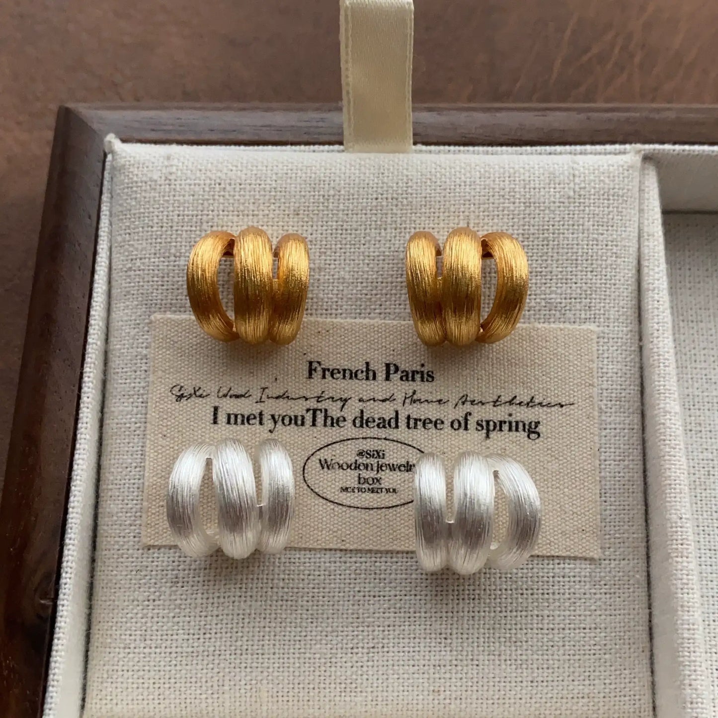 Gold-tone and silver-tone triple band earrings arranged together in a jewelry box.