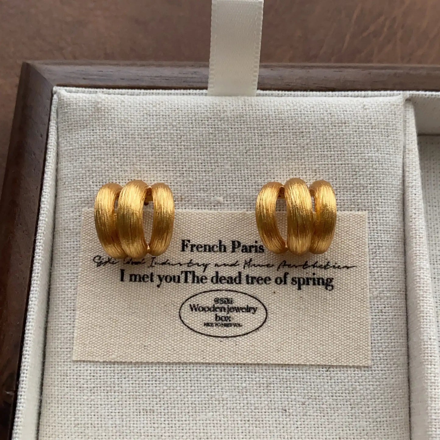 Close-up of textured gold triple hoop earrings with a brushed metal finish.