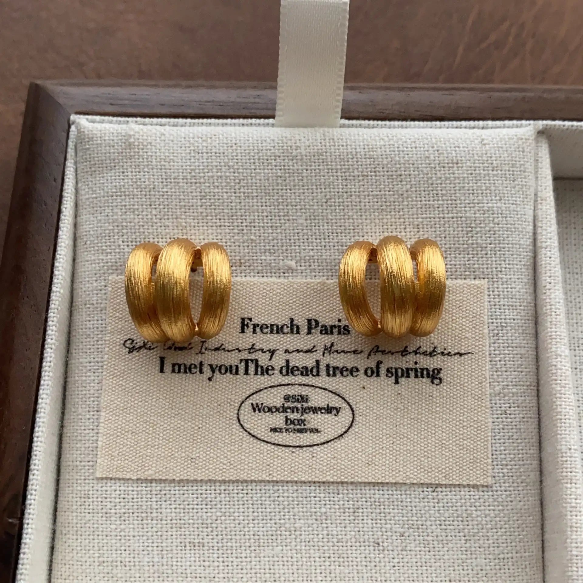 Close-up of textured gold triple hoop earrings with a brushed metal finish.