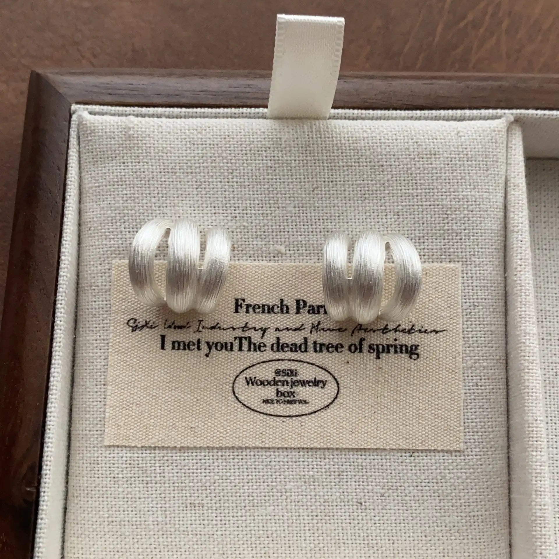 Silver brushed metal C-hoop earrings displayed on a neutral linen background.