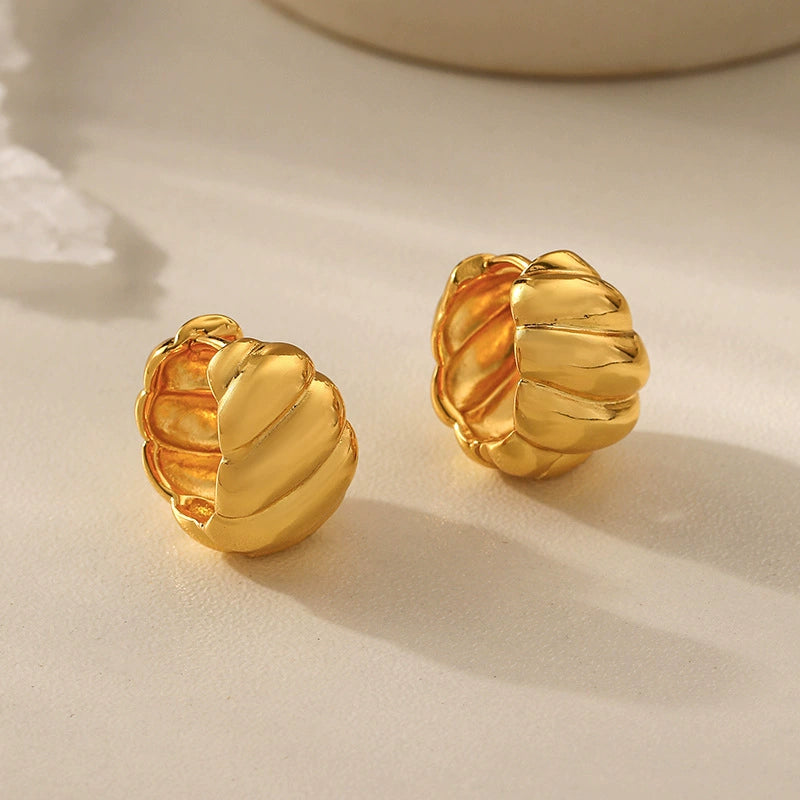 Gold tone croissant hoop earrings with sculptural ridged design on a neutral background
