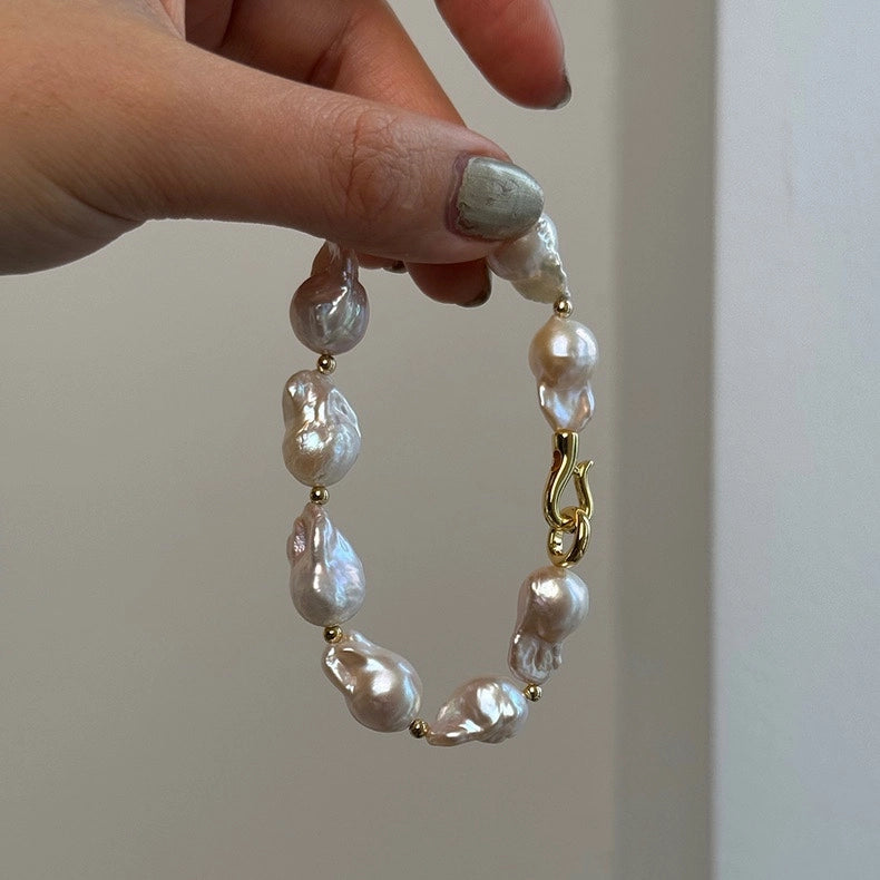 Hand holding a fishtail baroque pearl bracelet with lustrous organic pearls and gold details
