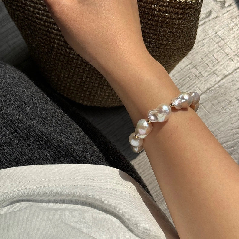 Large baroque pearl statement bracelet worn on the wrist with an elegant neutral outfit