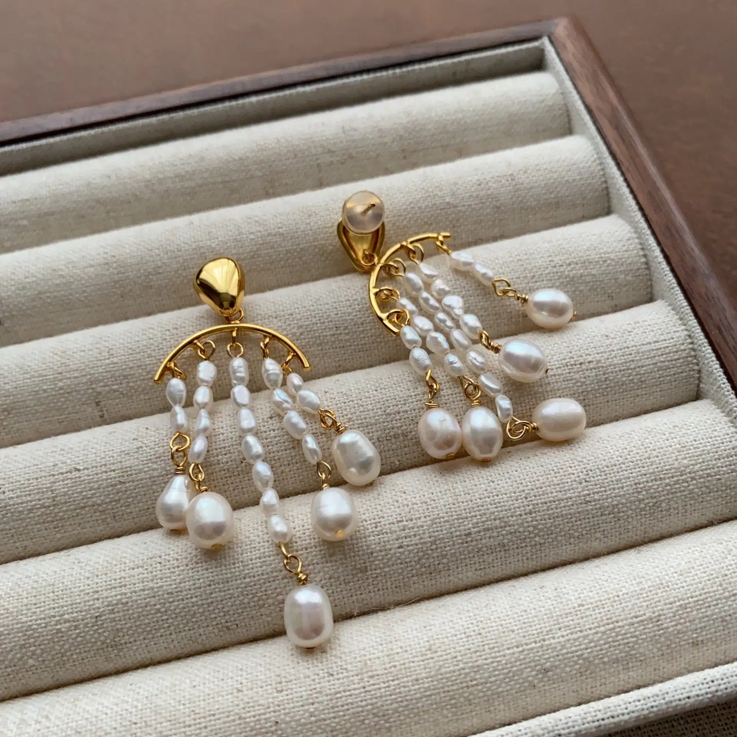 Angled view of gold-plated dangle earrings with layered pearl strands