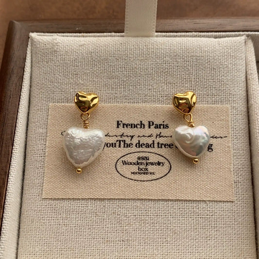 Heart baroque pearl earrings with gold-tone studs displayed on a beige linen jewelry card.