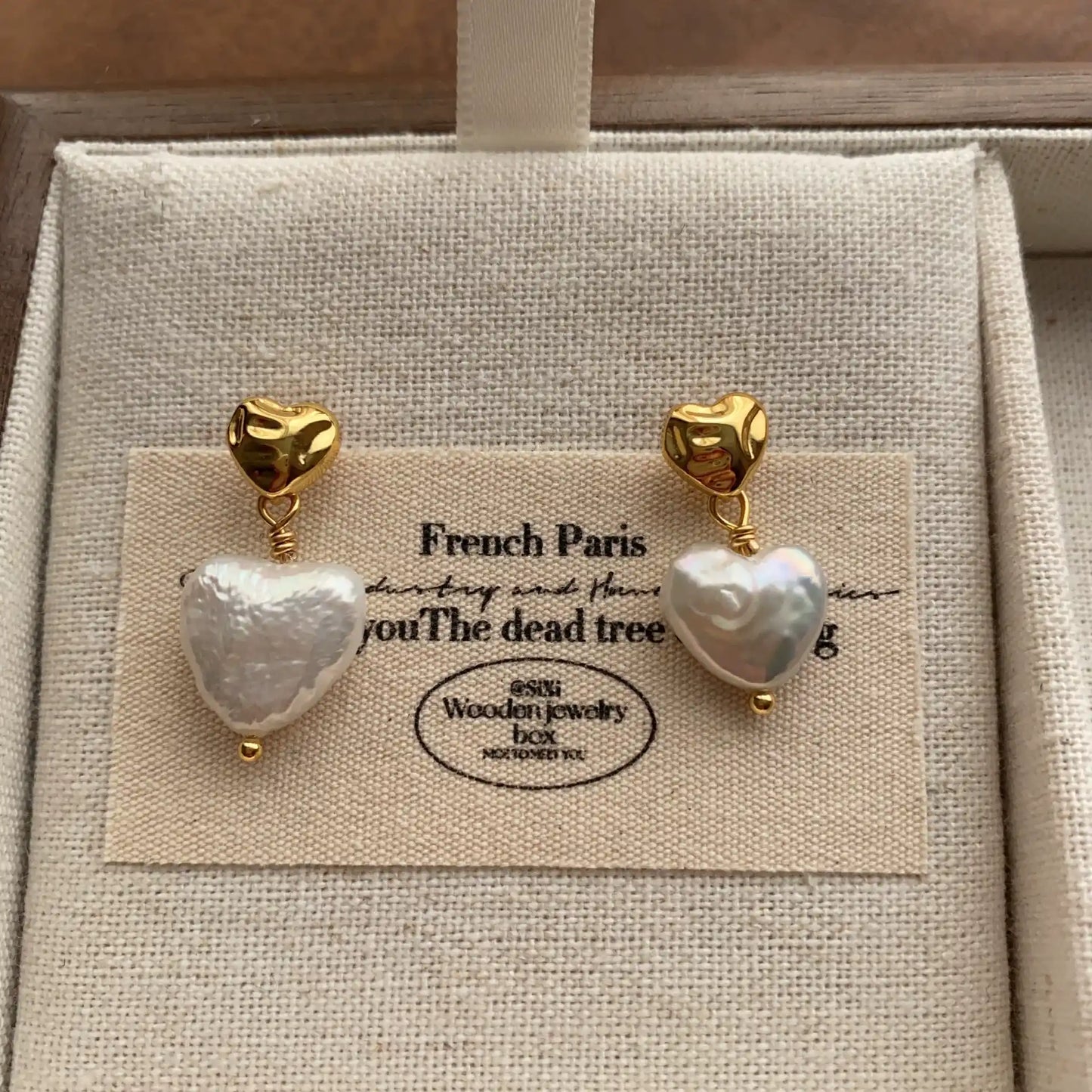 Close-up of heart-shaped baroque pearl drop earrings with sculptural gold-tone studs.