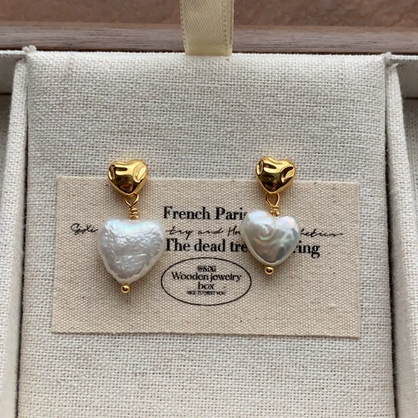 Gold-tone heart stud earrings with irregular white baroque pearl drops in a jewelry box.