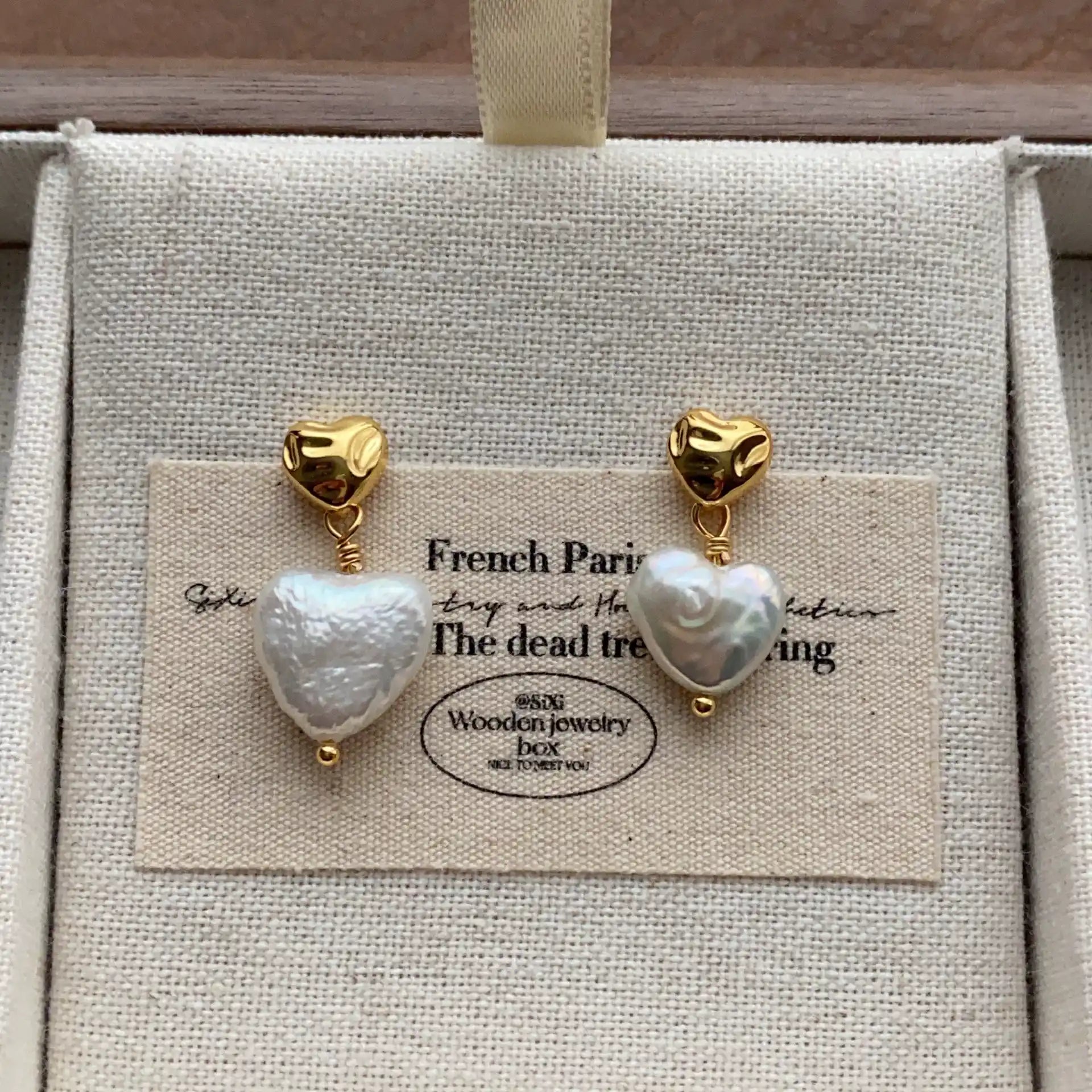 Gold-tone heart stud earrings with irregular white baroque pearl drops in a jewelry box.