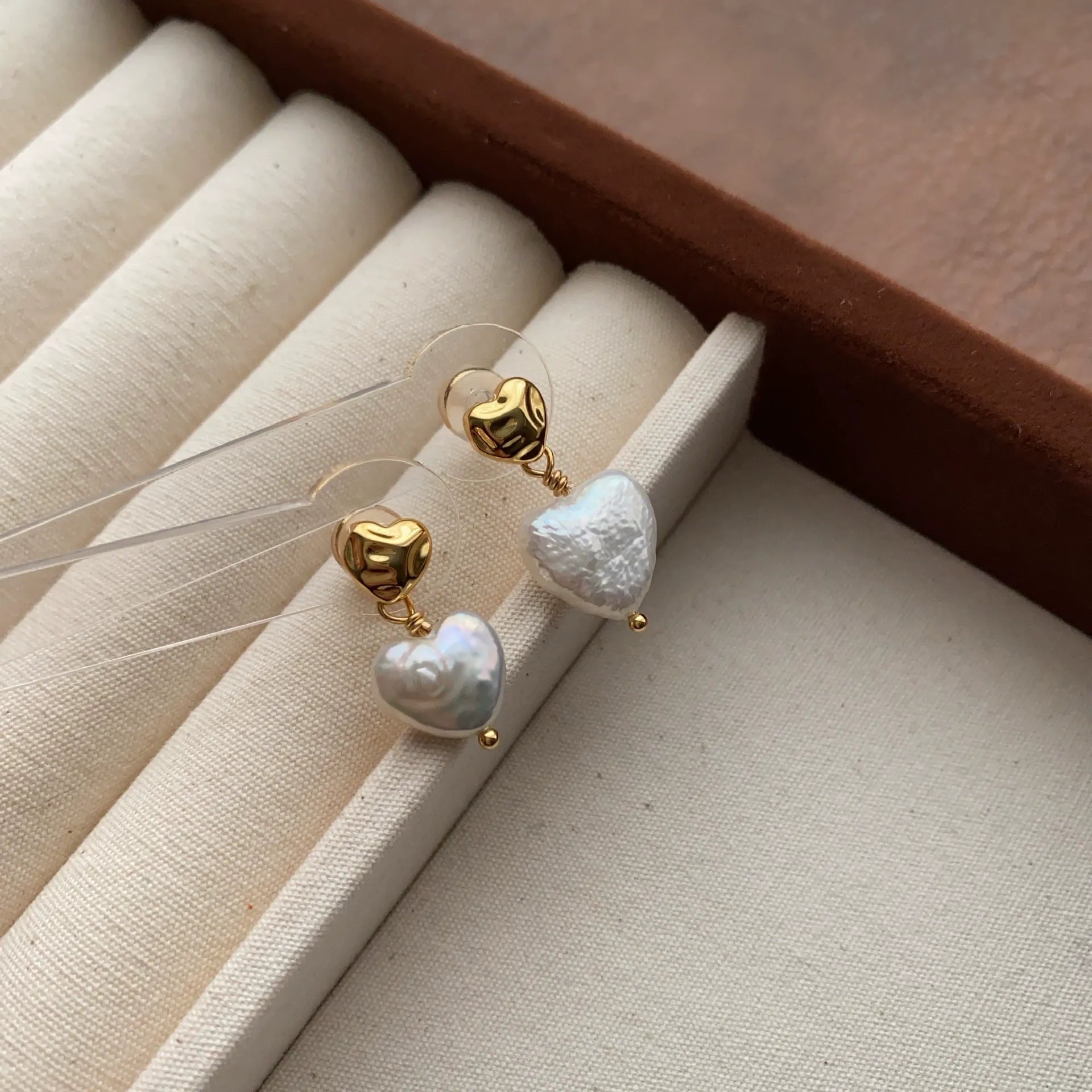 Heart baroque pearl earrings arranged on a cream velvet jewelry tray with gold-tone details.