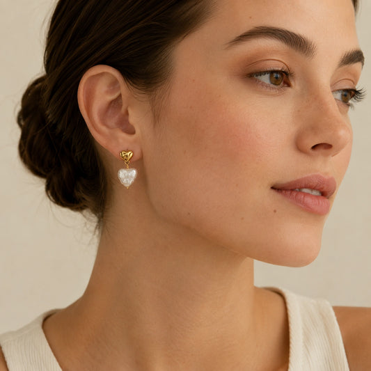 Model wearing petite heart baroque pearl drop earrings with gold-tone studs and swept-back hair.