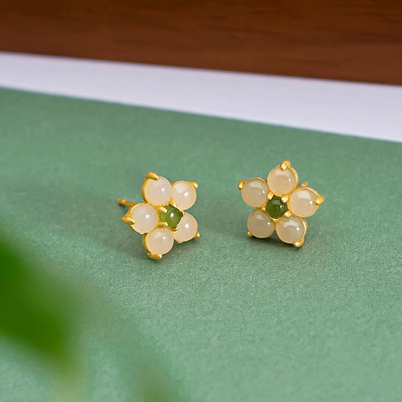 Minimalist jade flower stud earrings in 925 silver on green fabric background.