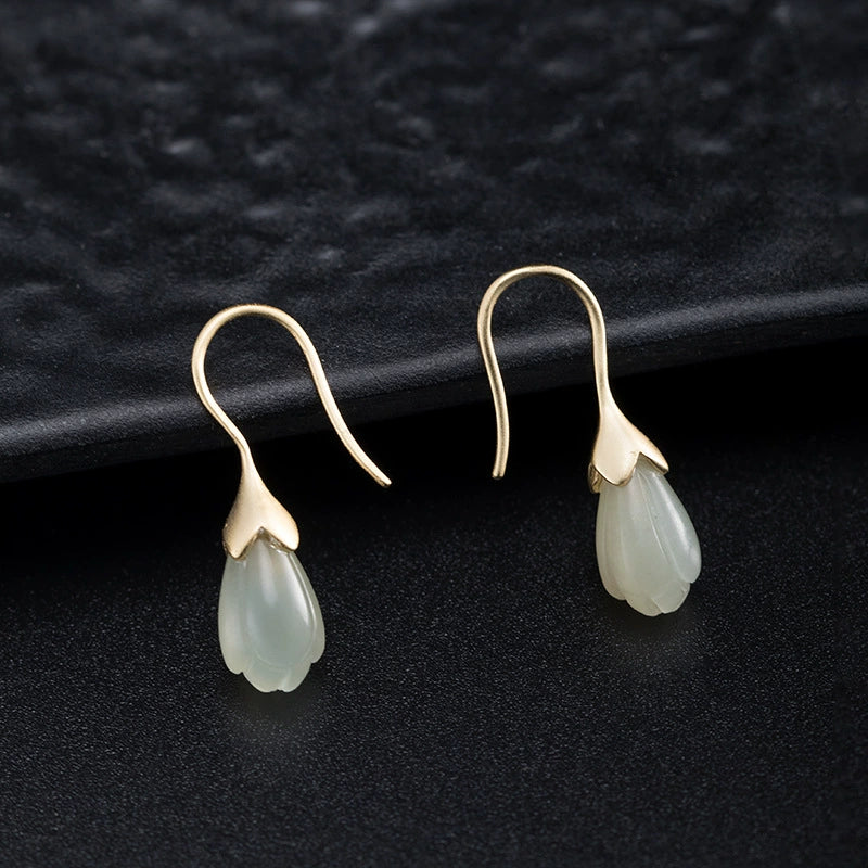 Hetian jade magnolia flower earrings in gold plated S925 silver on black textured background.