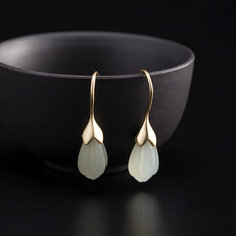 Natural Hetian jade drop earrings with gold plated sterling silver hooks beside black ceramic cup.