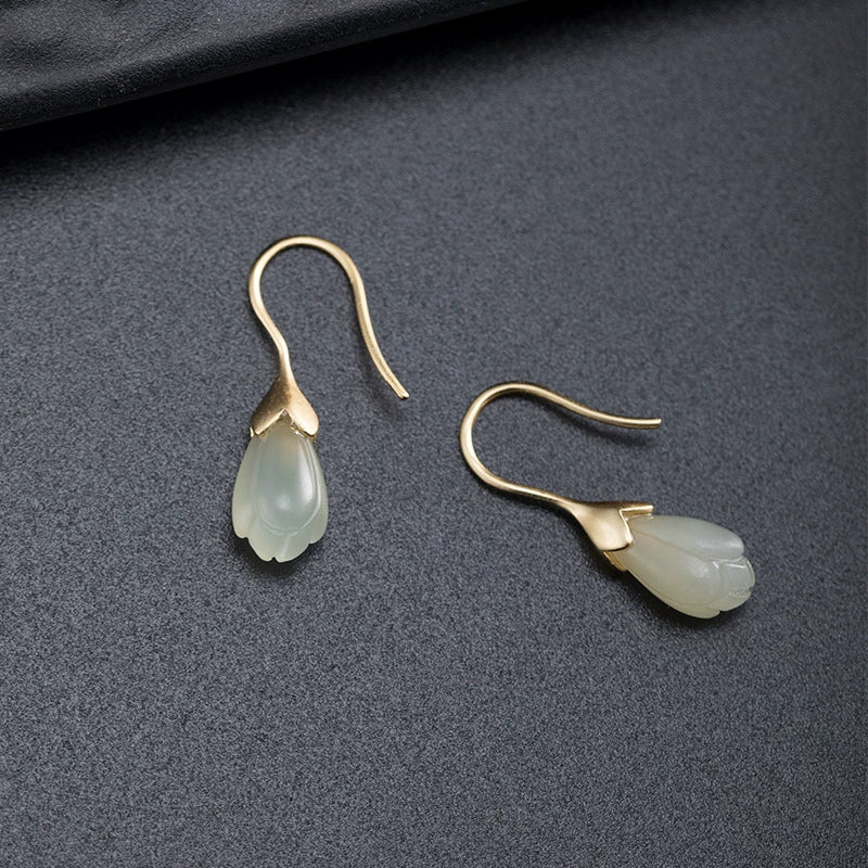 Pale jade green magnolia flower earrings in S925 silver displayed on matte black surface.