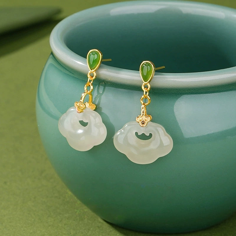 White jade ruyi lock earrings with green jade studs and gold-tone S925 silver beside teal ceramic cup.