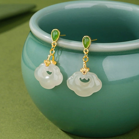 White jade ruyi lock earrings with green jade studs and gold-tone S925 silver beside teal ceramic cup.