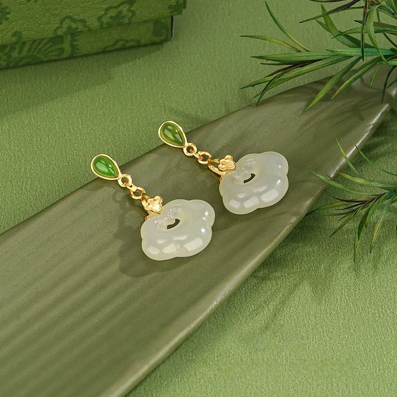 Natural Hetian jade dangle earrings with ruyi lock design on green background.