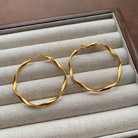Gold Möbius strip twisted hoop earrings displayed on a neutral jewelry tray