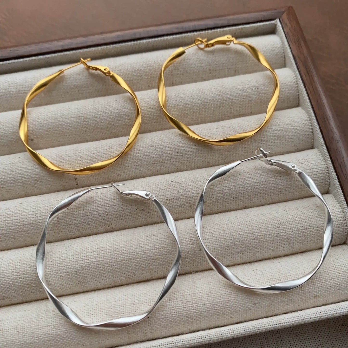 Gold and silver geometric twisted hoop earrings shown together on a jewelry tray