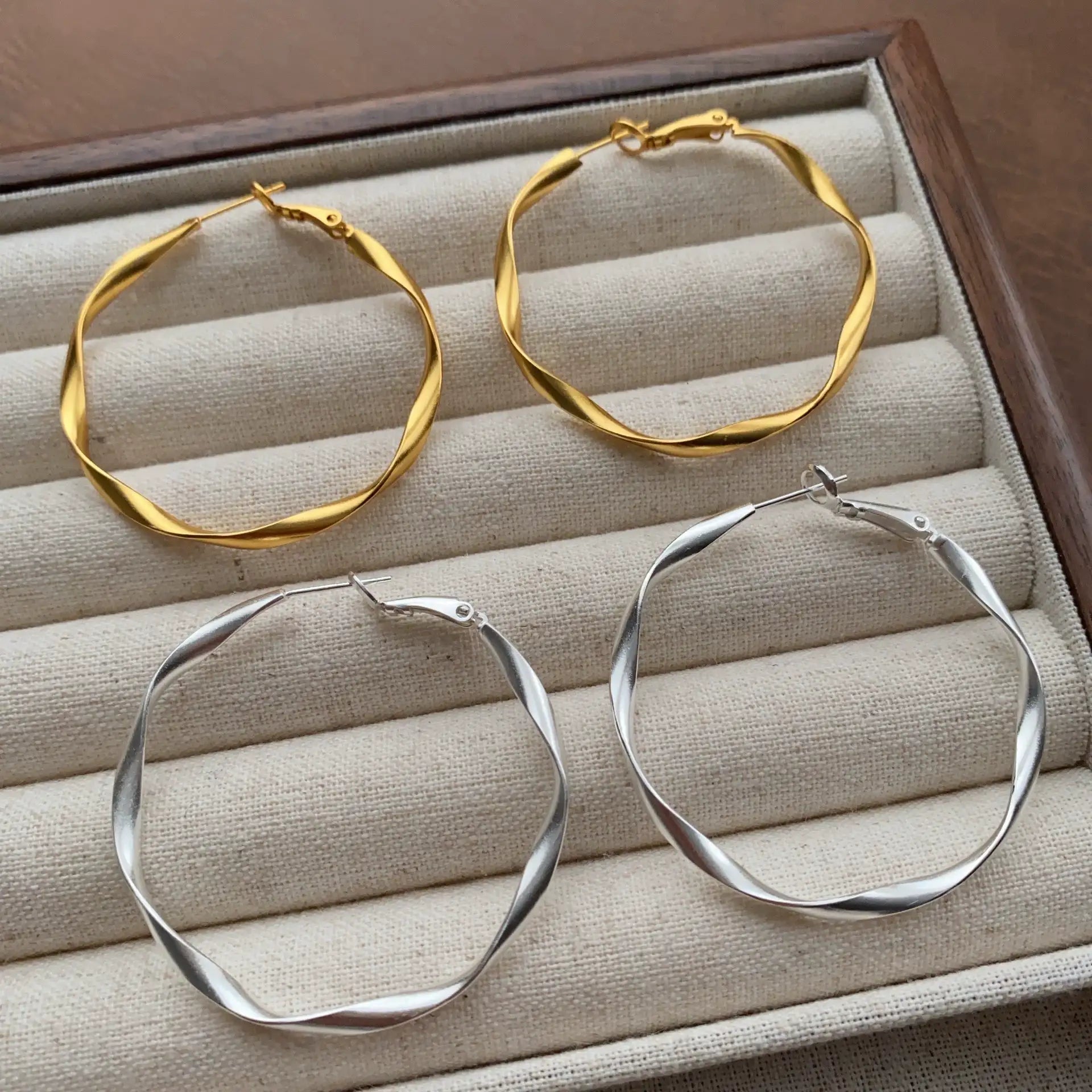 Gold and silver geometric twisted hoop earrings shown together on a jewelry tray