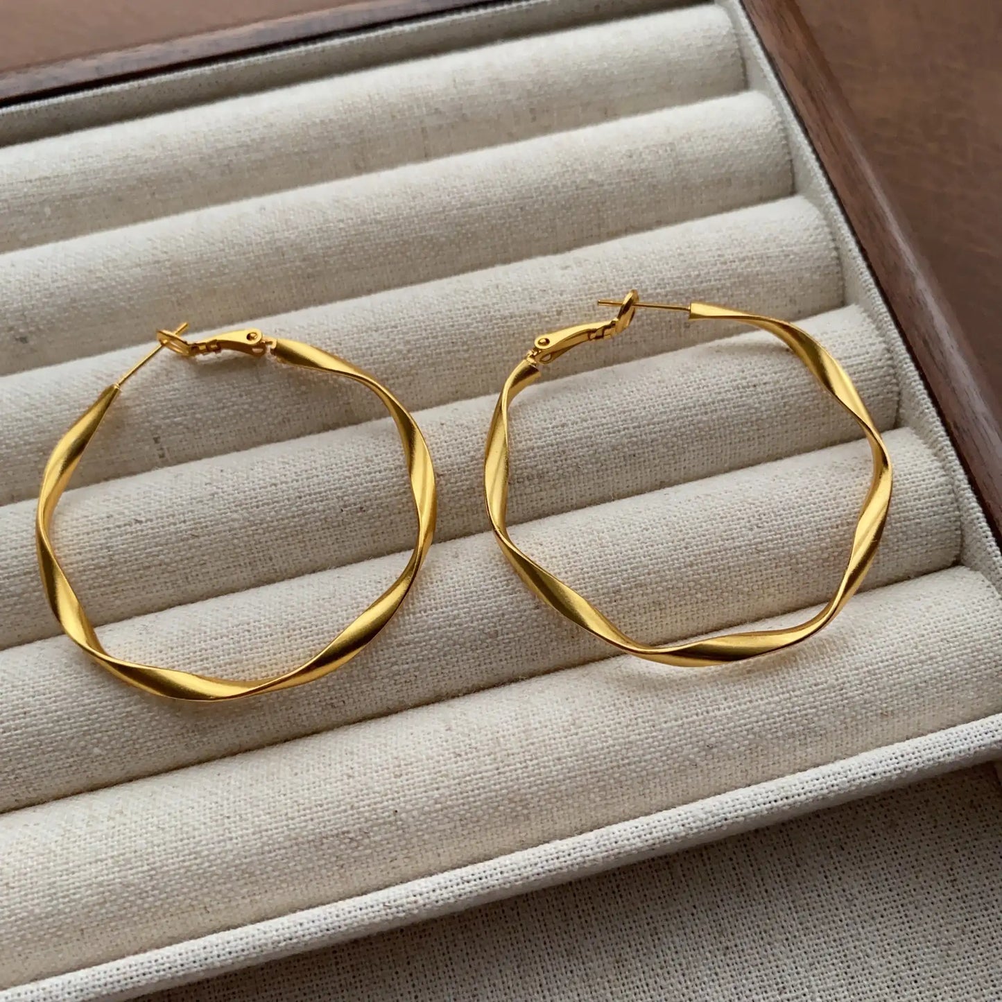 Close-up of gold wavy hoop earrings with a polished Möbius-inspired design