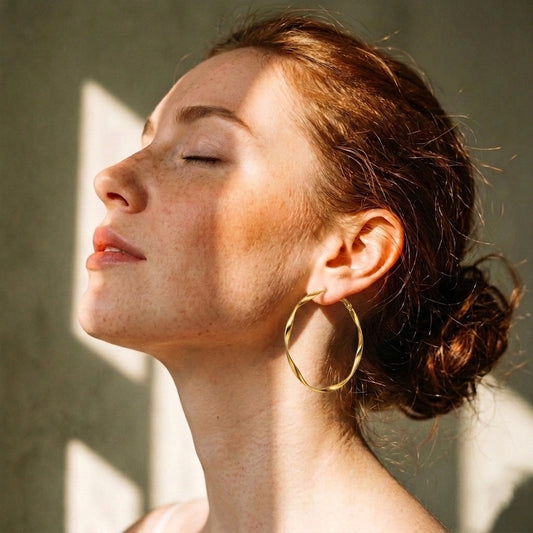Model wearing gold Möbius strip hoop earrings in warm natural light